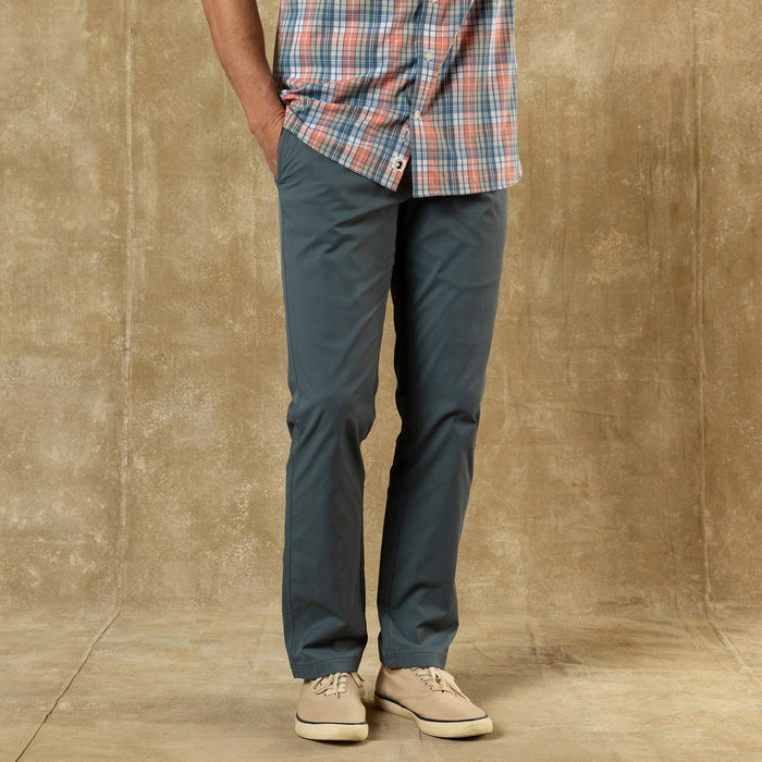 Dark blue-gray chino pants worn with plaid shirt and canvas sneakers, lower body view