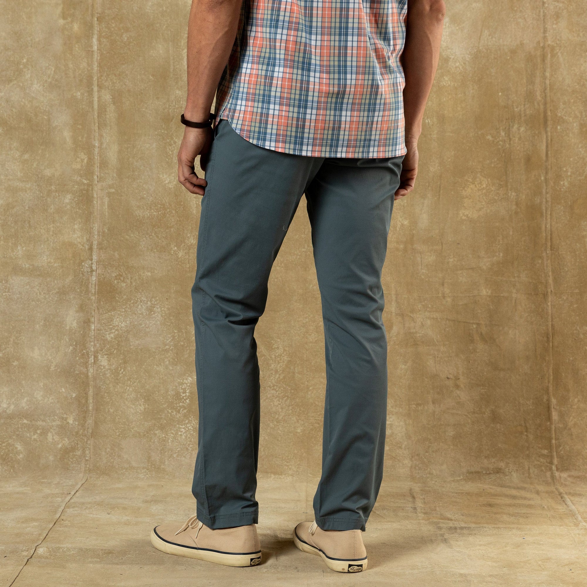 Men's blue-gray chino pants shown from back view with plaid shirt and canvas shoes