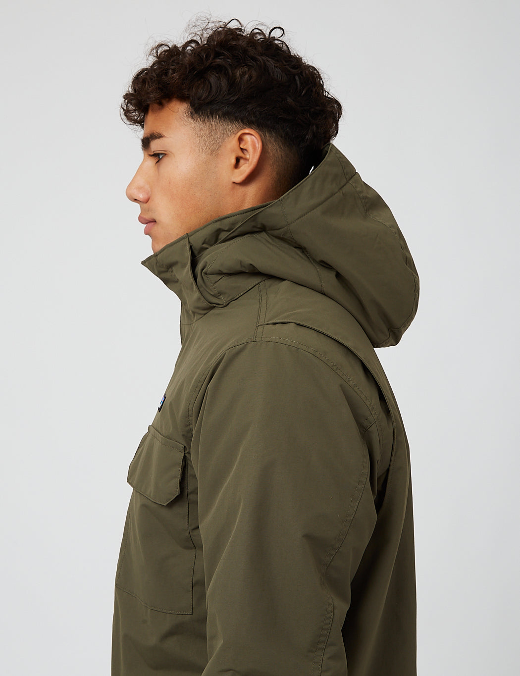 Men's hooded parka in olive green, side profile close-up showing hood and chest pocket detail