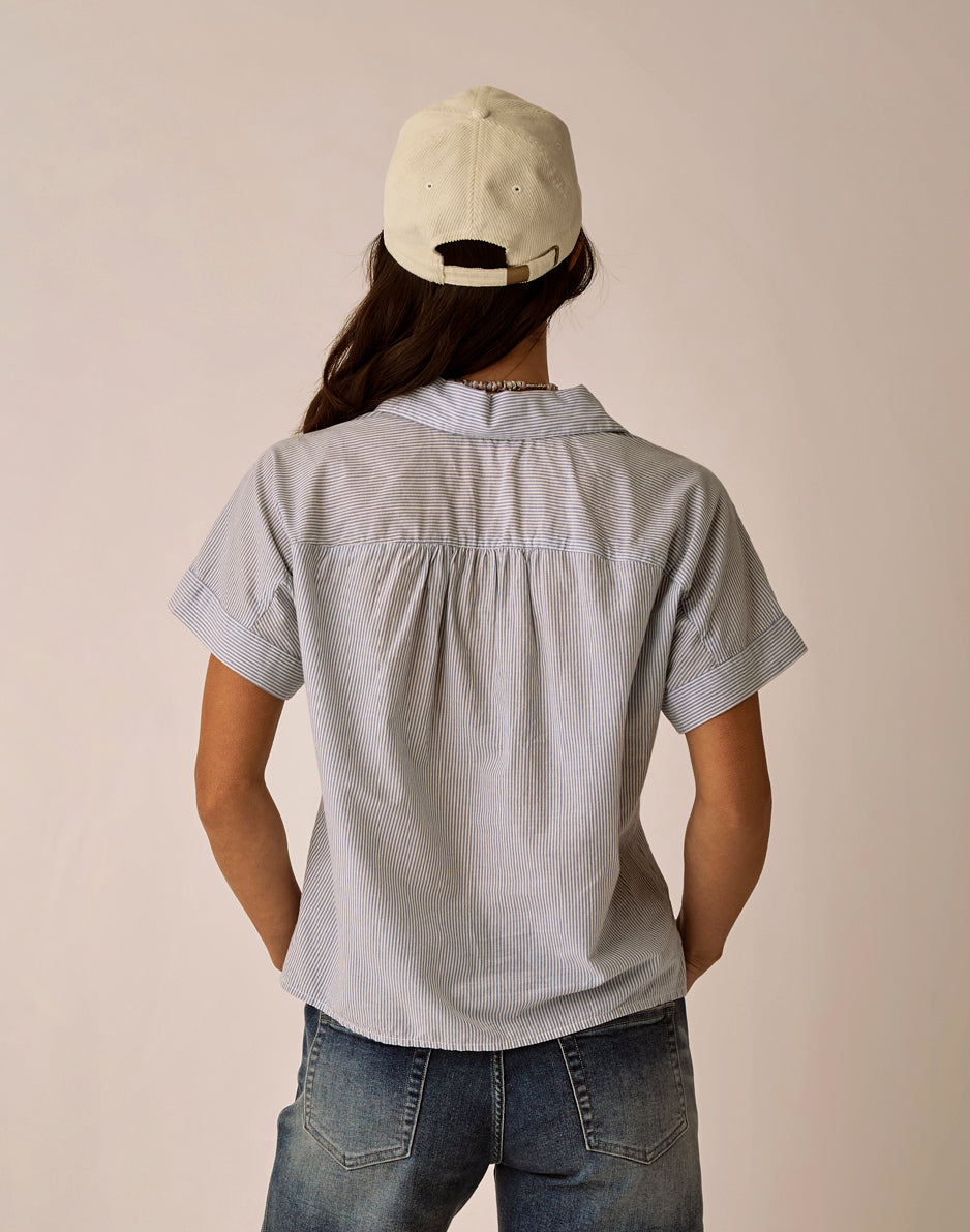 Gray pinstriped short sleeve collared top shown from back on model with cap
