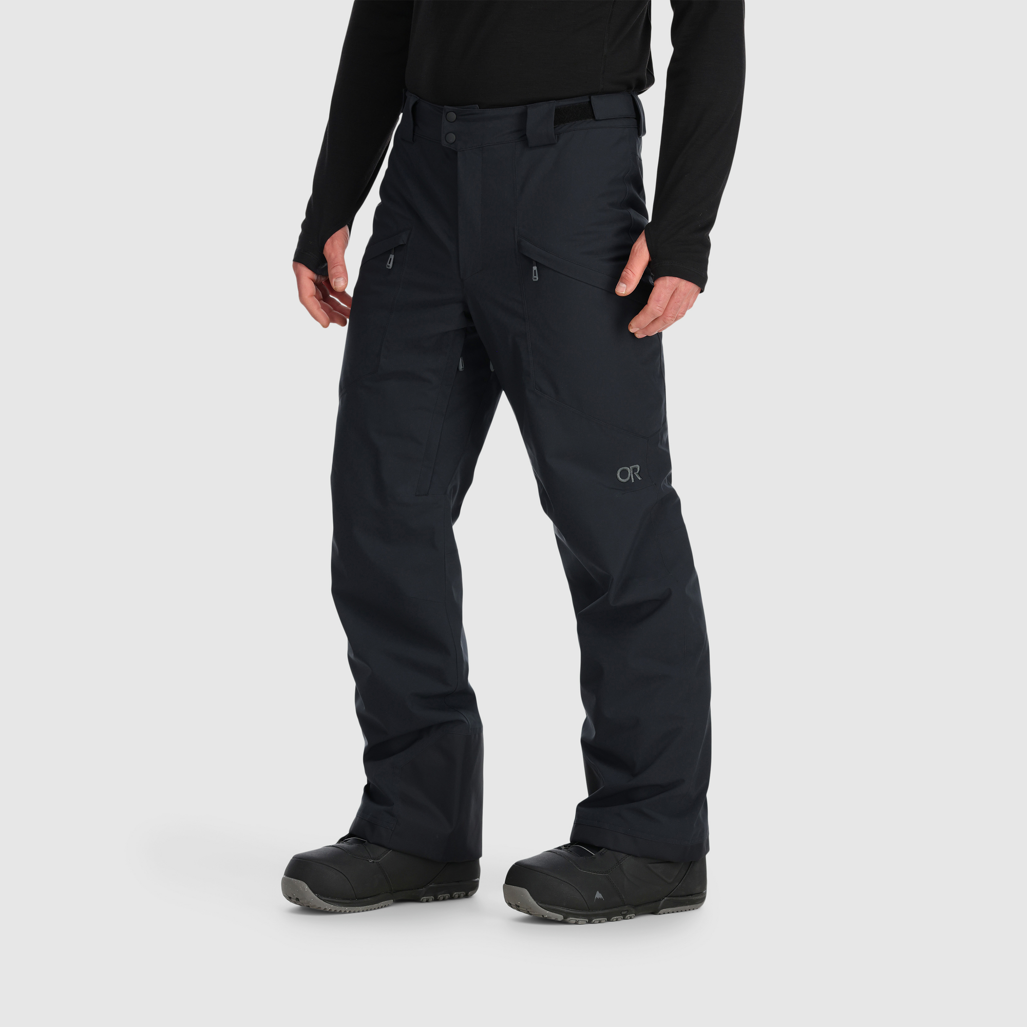 Black snow pants with multiple zippered pockets, worn on model with snowboard boots, front view