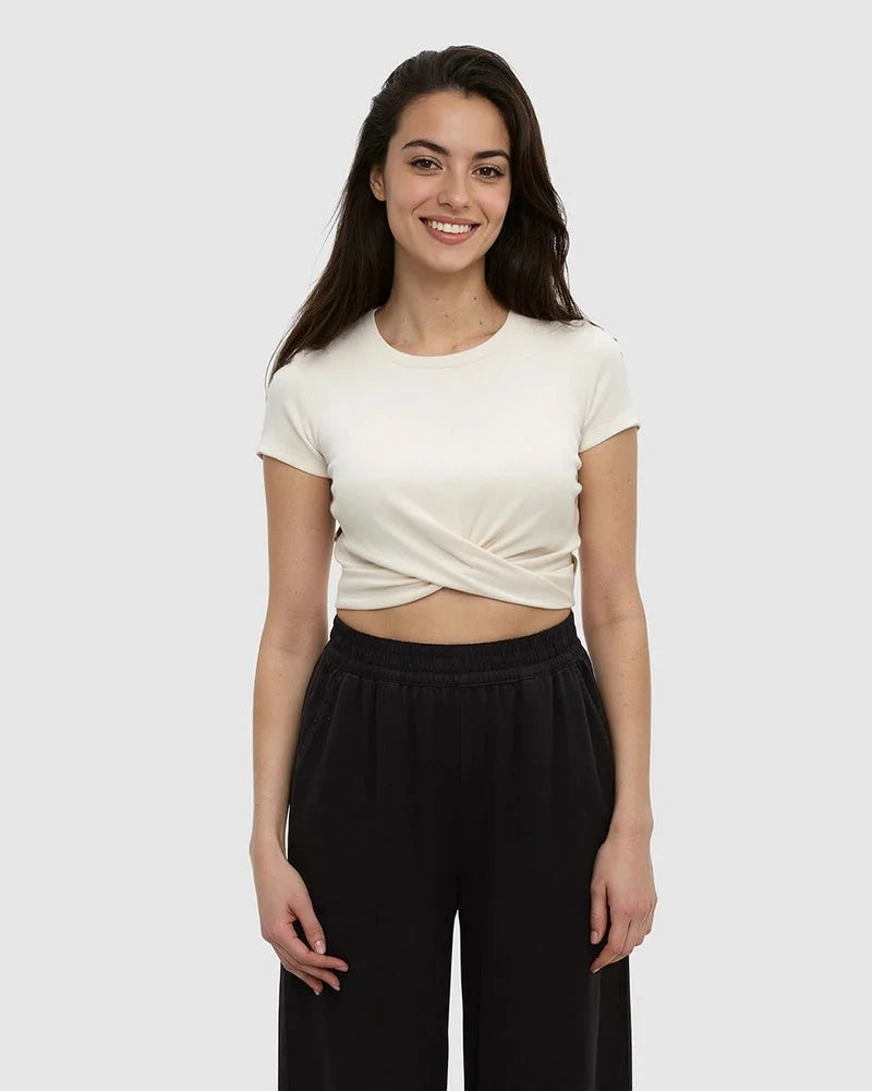 Woman wearing cream colored short-sleeve crop top with twisted front detail and black pants