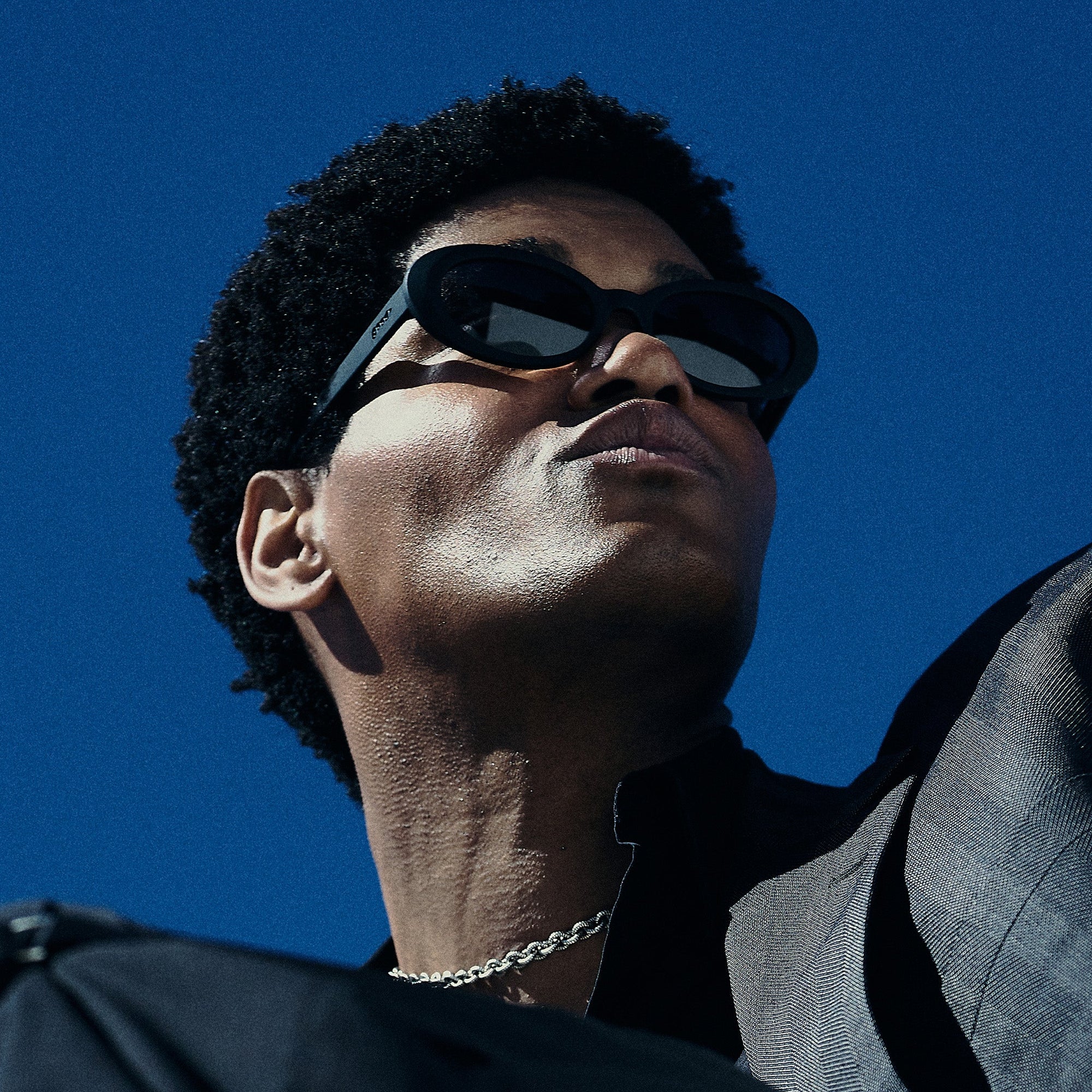 Black wraparound sunglasses worn by person looking upward against blue sky background