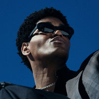 Black wraparound sunglasses worn by person looking upward against blue sky background