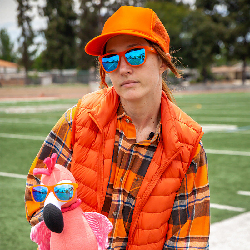 Blue mirrored sunglasses worn by person in orange outfit on sports field