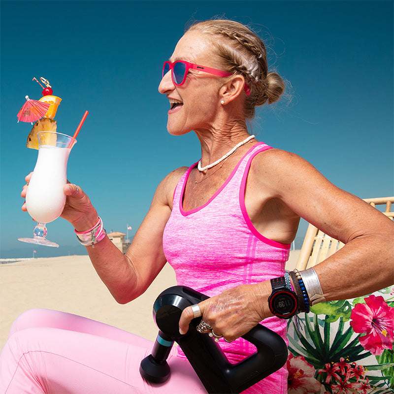 Pink-framed sunglasses with dark lenses worn by woman holding tropical drink on beach