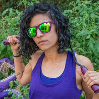Purple framed sunglasses with green mirrored lenses worn by woman in lifestyle setting