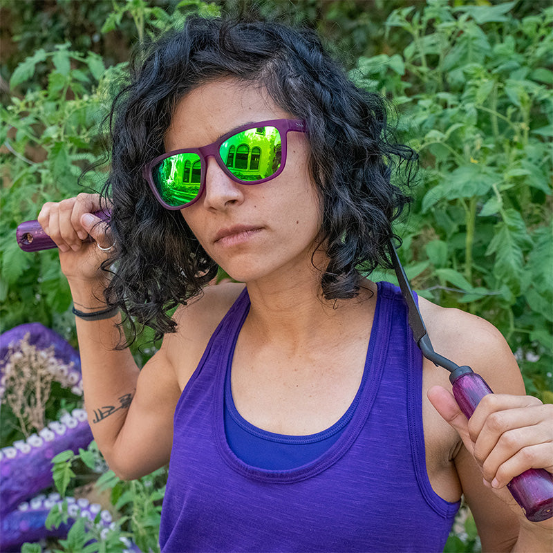 Purple framed sunglasses with green mirrored lenses worn by woman in lifestyle setting