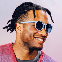 Light blue round sunglasses with dark lenses worn by smiling man in lifestyle photo