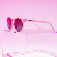 Pink round sunglasses with dark purple lenses displayed on clear acrylic stand