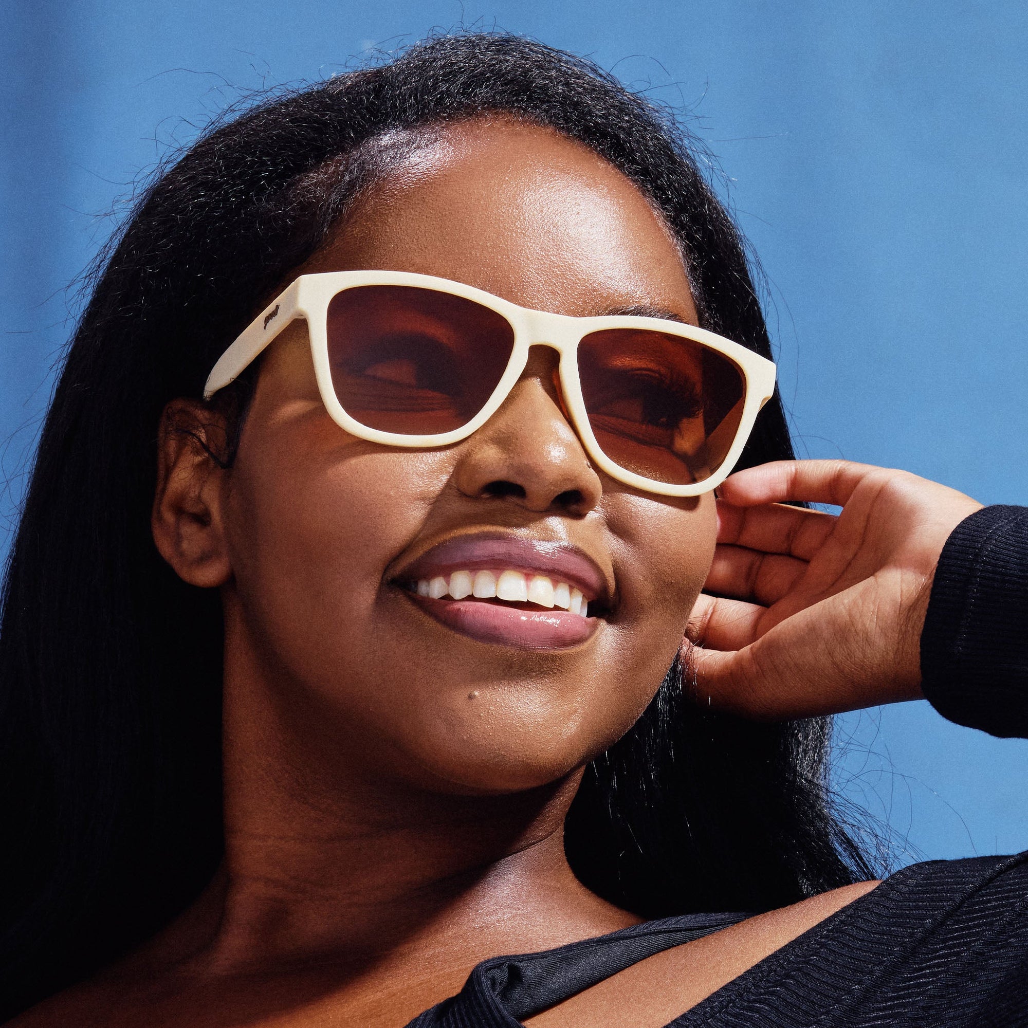 Woman wearing cream-colored sunglasses with gradient lenses against blue sky background