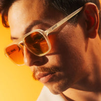 Cream-colored sunglasses with amber lenses worn by person in warm golden lighting
