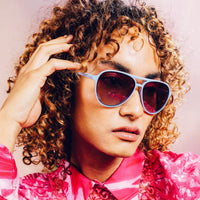 Light blue aviator sunglasses with dark gradient lenses worn by person with curly hair