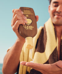Person applying sunscreen lotion from brown squeeze bottle onto palm of hand