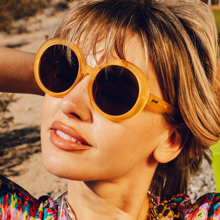 Woman wearing translucent orange round sunglasses, looking upward in natural lighting