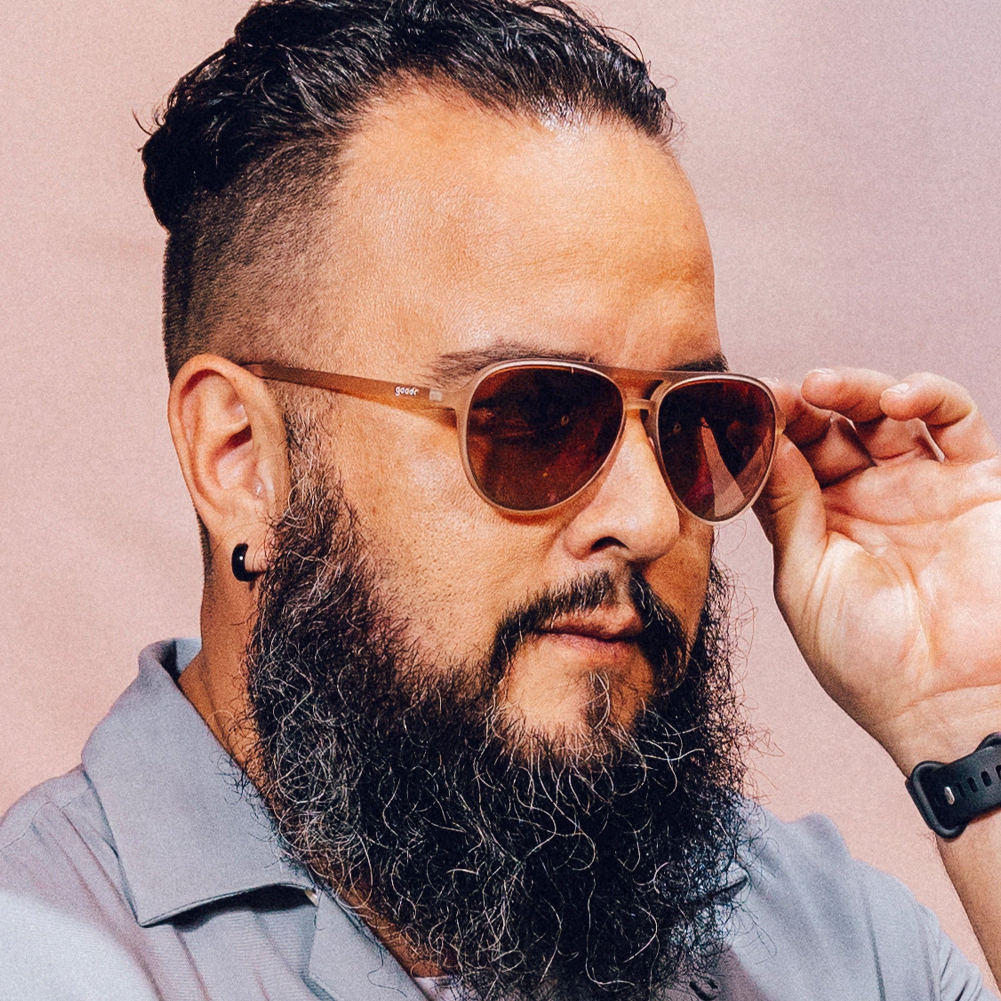 Aviator-style sunglasses with translucent brown frames worn by bearded man adjusting them with hand
