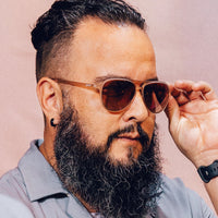 Aviator-style sunglasses with translucent brown frames worn by bearded man adjusting them with hand