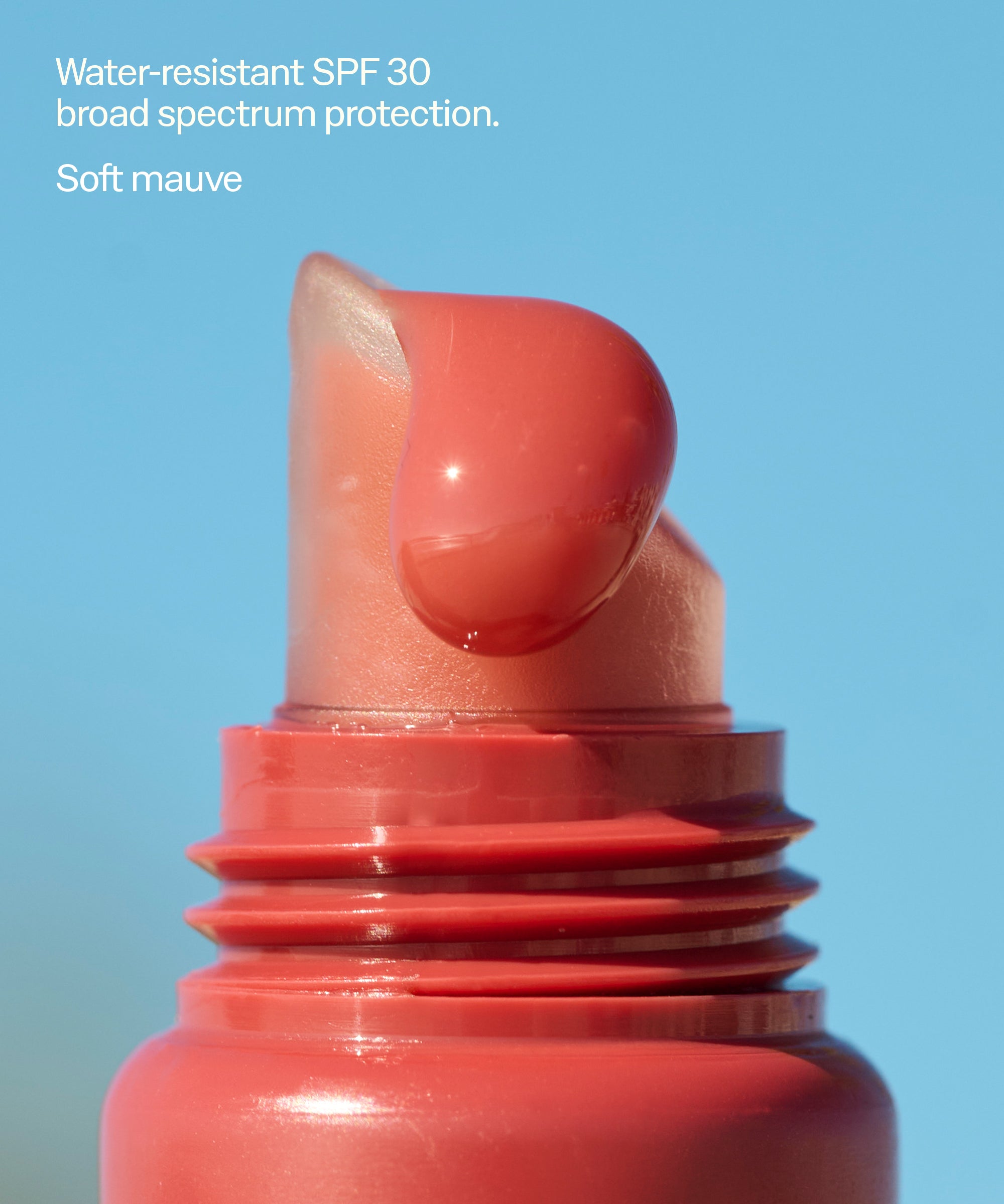 Coral-red tinted lip balm stick with SPF 30, shown extended from tube against blue background