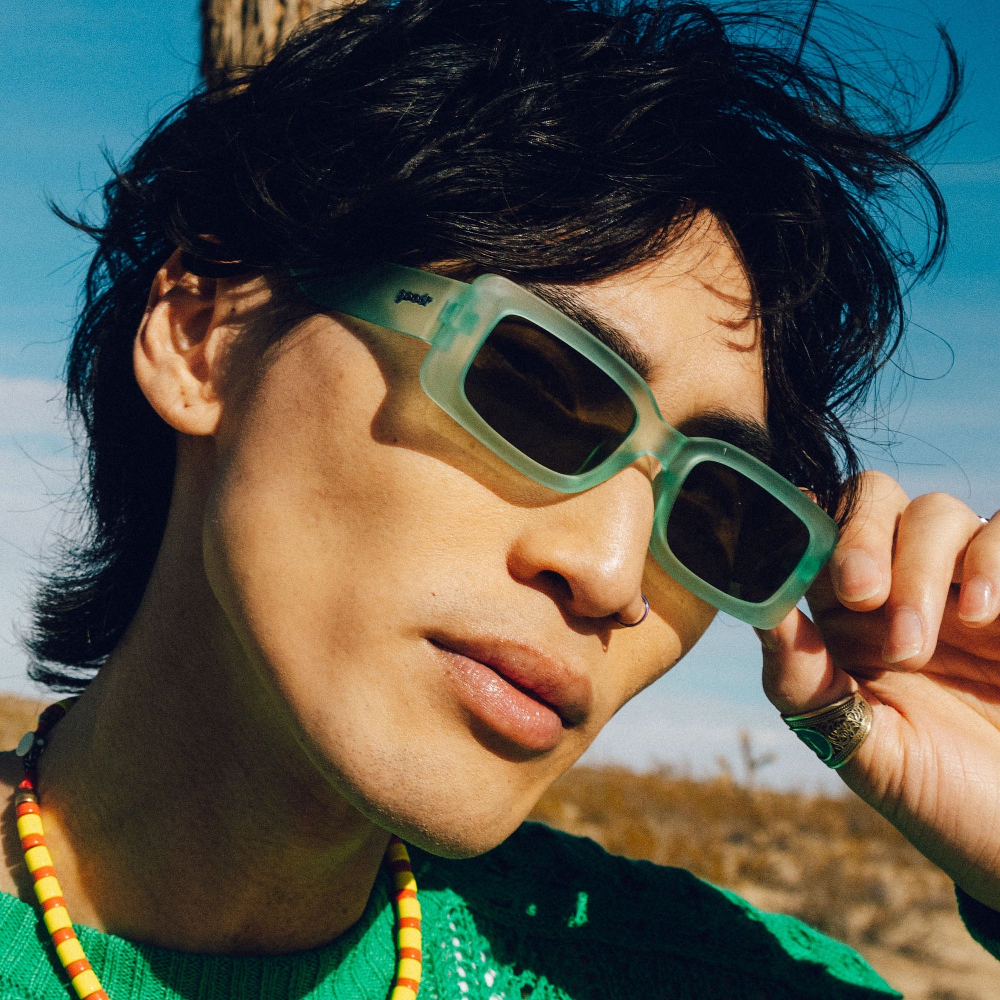 Person wearing mint green rectangular sunglasses outdoors, hand adjusting frame