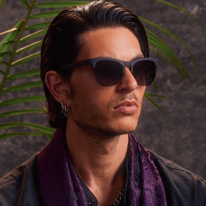 Man wearing matte blue sunglasses with dark lenses in tropical lifestyle setting