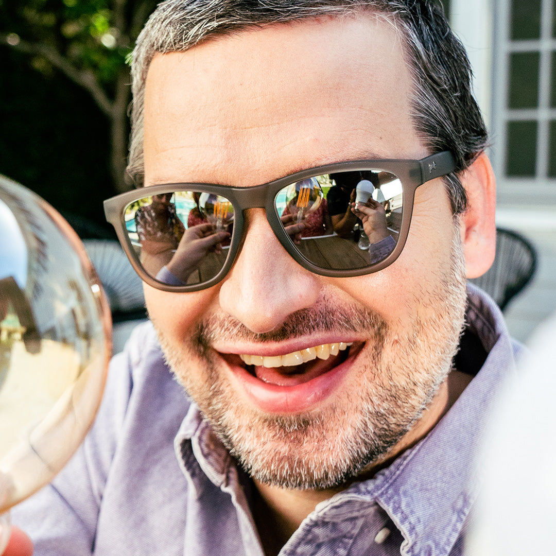 Dark sunglasses with mirrored golden brown lenses worn by smiling man outdoors