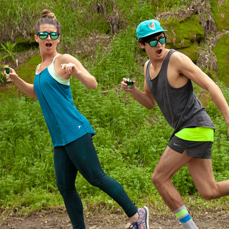 Two runners wearing teal-green sunglasses jogging outdoors on natural trail