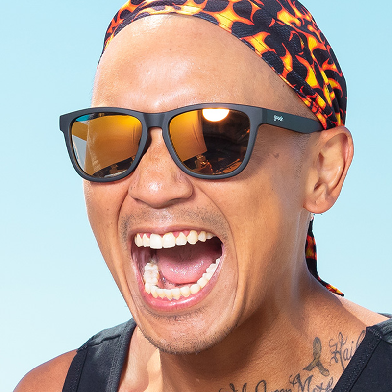 Dark frame sunglasses with orange reflective lenses worn by smiling person outdoors
