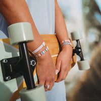 Striped hair tie bracelets worn on wrist of person holding a bamboo longboard skateboard