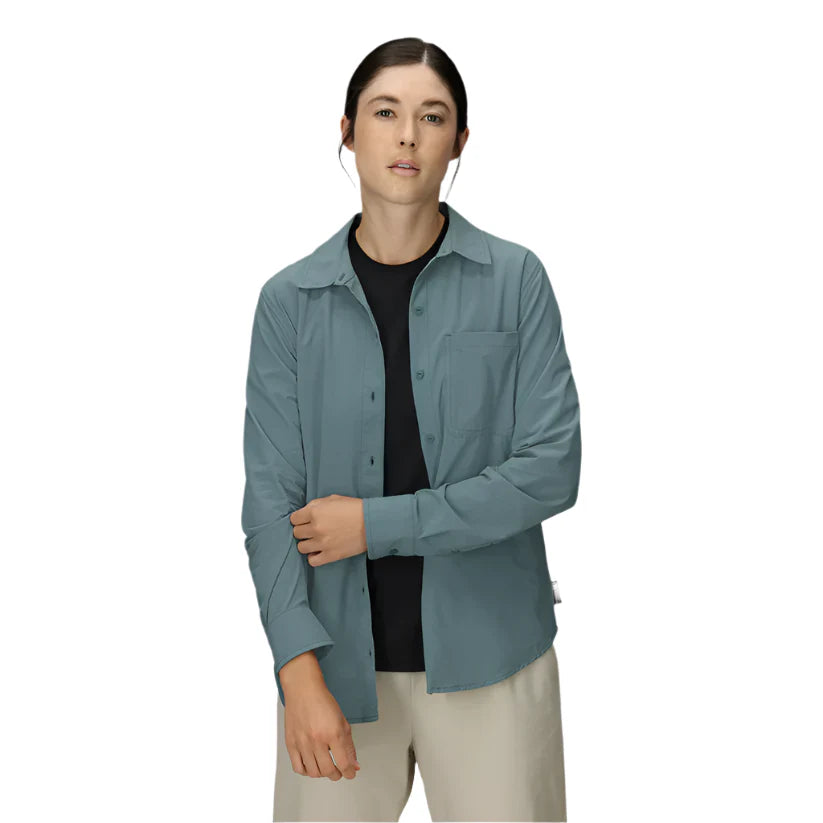 Woman wearing dusty blue-green long sleeve button-up shirt over black top with beige pants