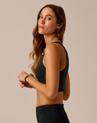 Women's black racerback crop top, side view, styled with black high-waist bottoms