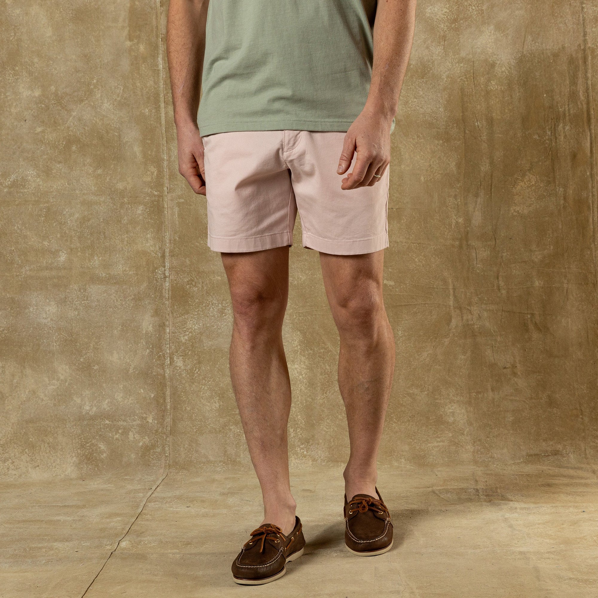 Light pink chino shorts worn with green t-shirt and brown boat shoes, studio shot