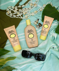 Three sunscreen lotion bottles in coral packaging with yellow caps displayed on turquoise towel