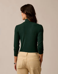 Women's long-sleeve turtleneck top in dark green, back view on model with khaki pants