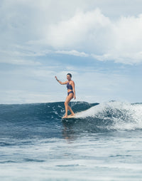 Woman surfing wearing navy patterned compression tankini top and matching bottoms