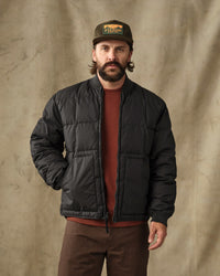 Men's black quilted puffer bomber jacket, front view, worn open over rust sweater