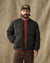 Men's black quilted puffer bomber jacket, front view, worn open over rust sweater
