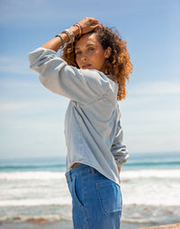 Women's lightweight denim pullover top in light wash, worn on-model at beach, three-quarter back view