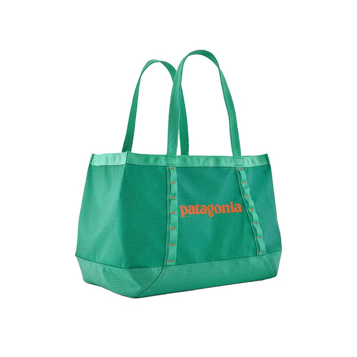 Teal tote bag with dual handles and front logo, angled view on white background