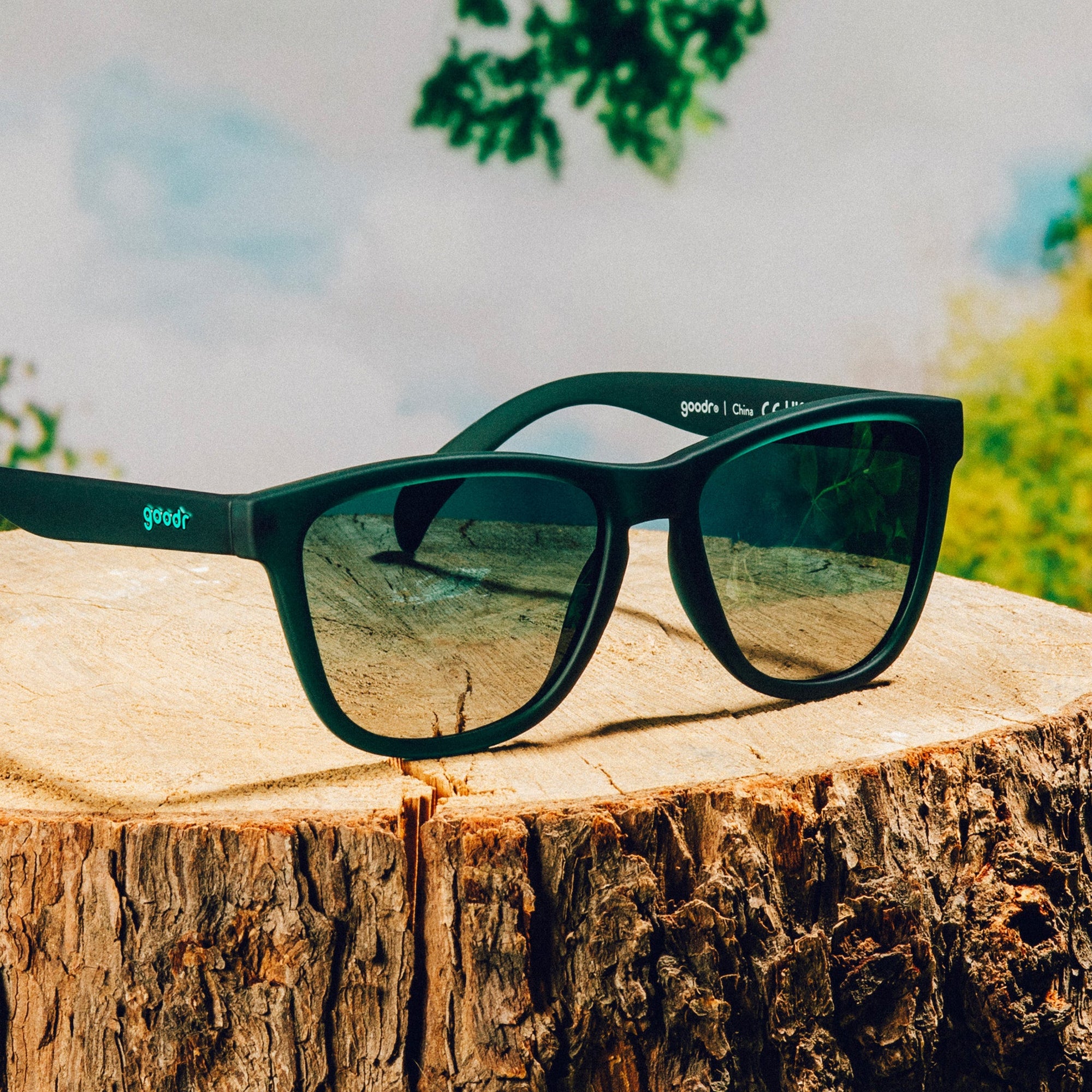 Dark green sunglasses with reflective lenses resting on wooden log surface outdoors
