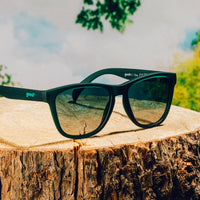 Dark green sunglasses with reflective lenses resting on wooden log surface outdoors