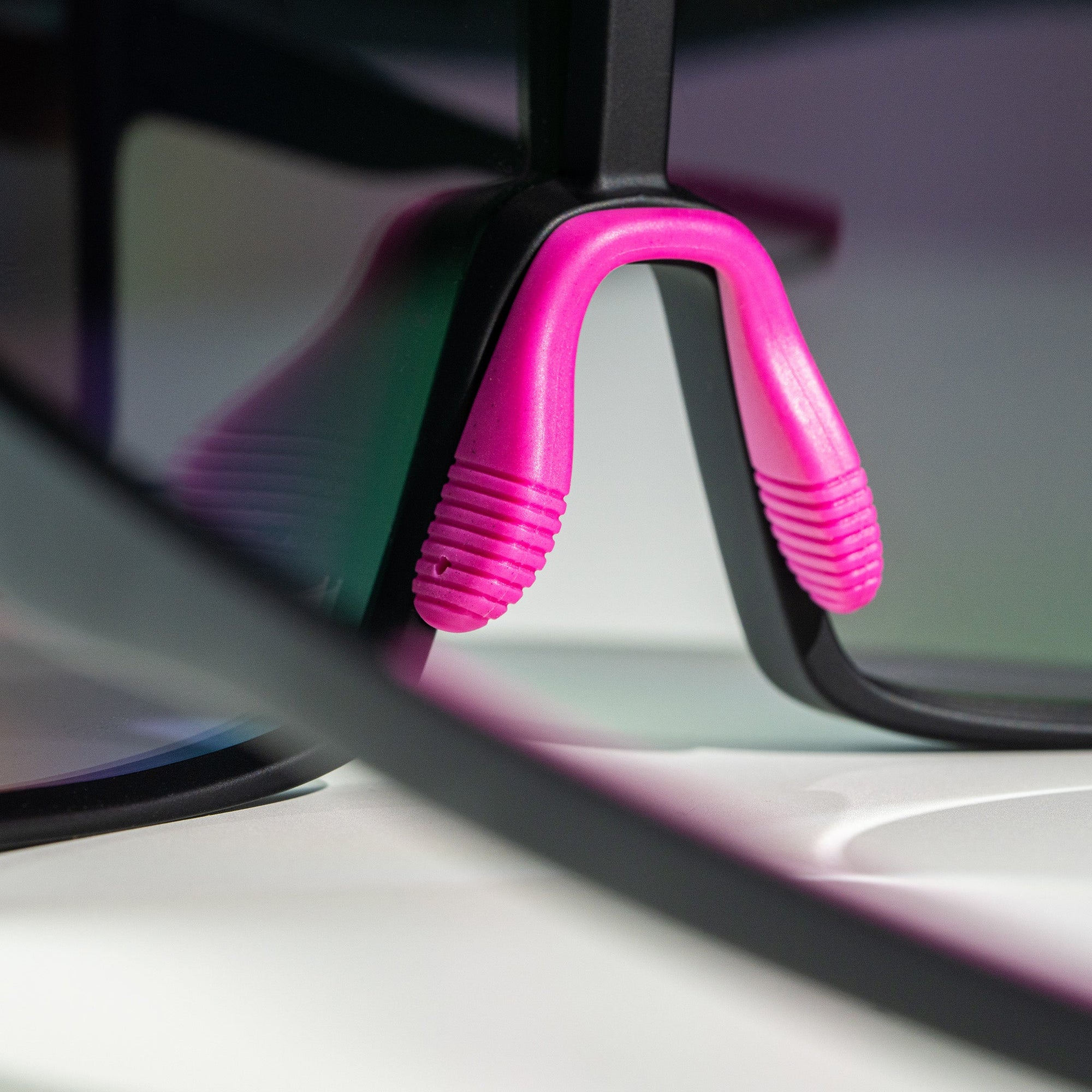 Black sunglasses with bright pink temple grips shown at an angle on white surface