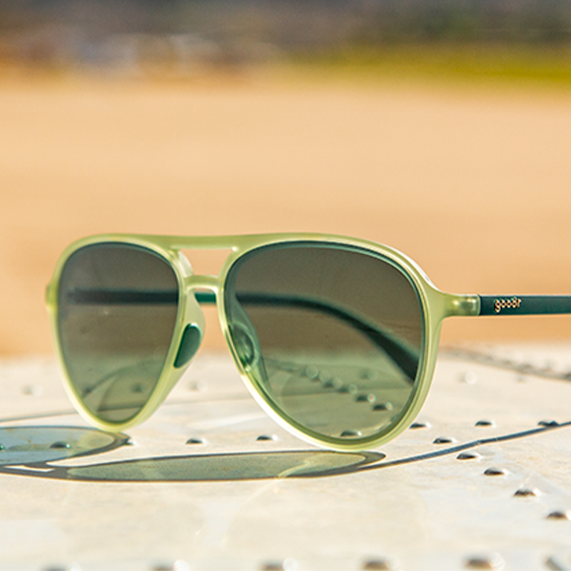 Light green aviator sunglasses with dark gradient lenses on sandy surface