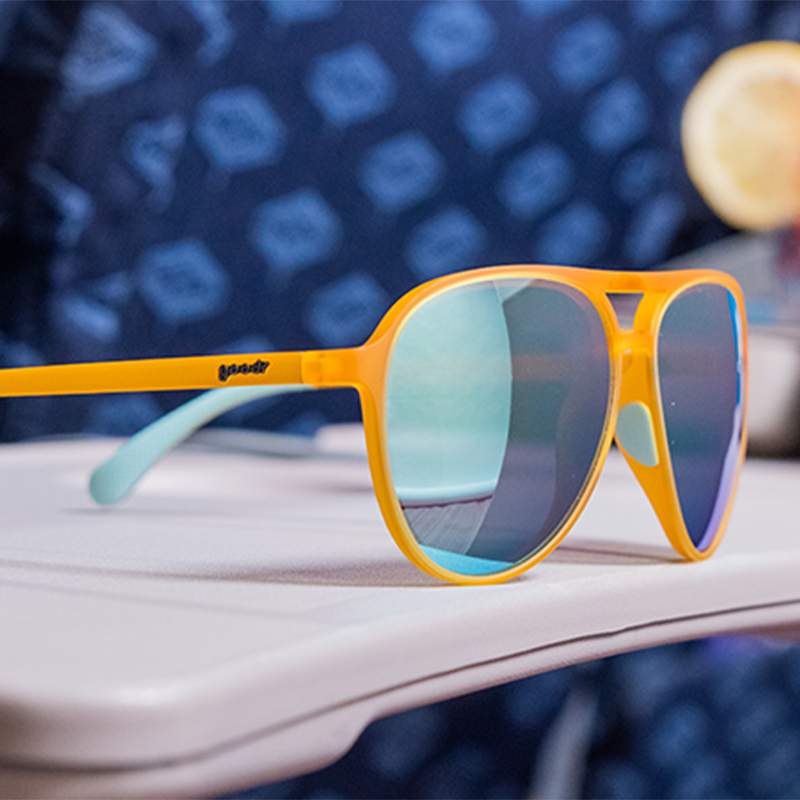 Orange aviator sunglasses with gradient mirrored lenses on wooden surface with blurred background