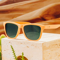 Peach colored sunglasses with dark green lenses resting on white stone surface