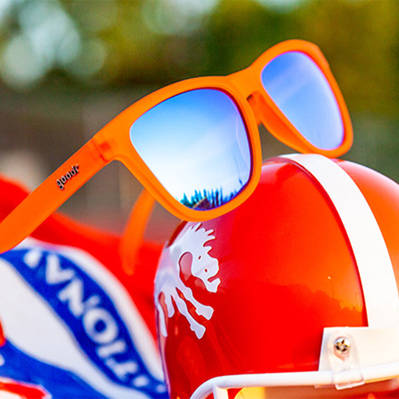 Bright orange sunglasses with blue mirrored lenses positioned on colorful packaging outdoors