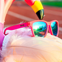 Hot pink sunglasses with blue mirrored lenses resting on white feathered surface