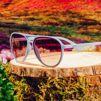 Aviator-style sunglasses with light colored frames displayed on wooden surface outdoors