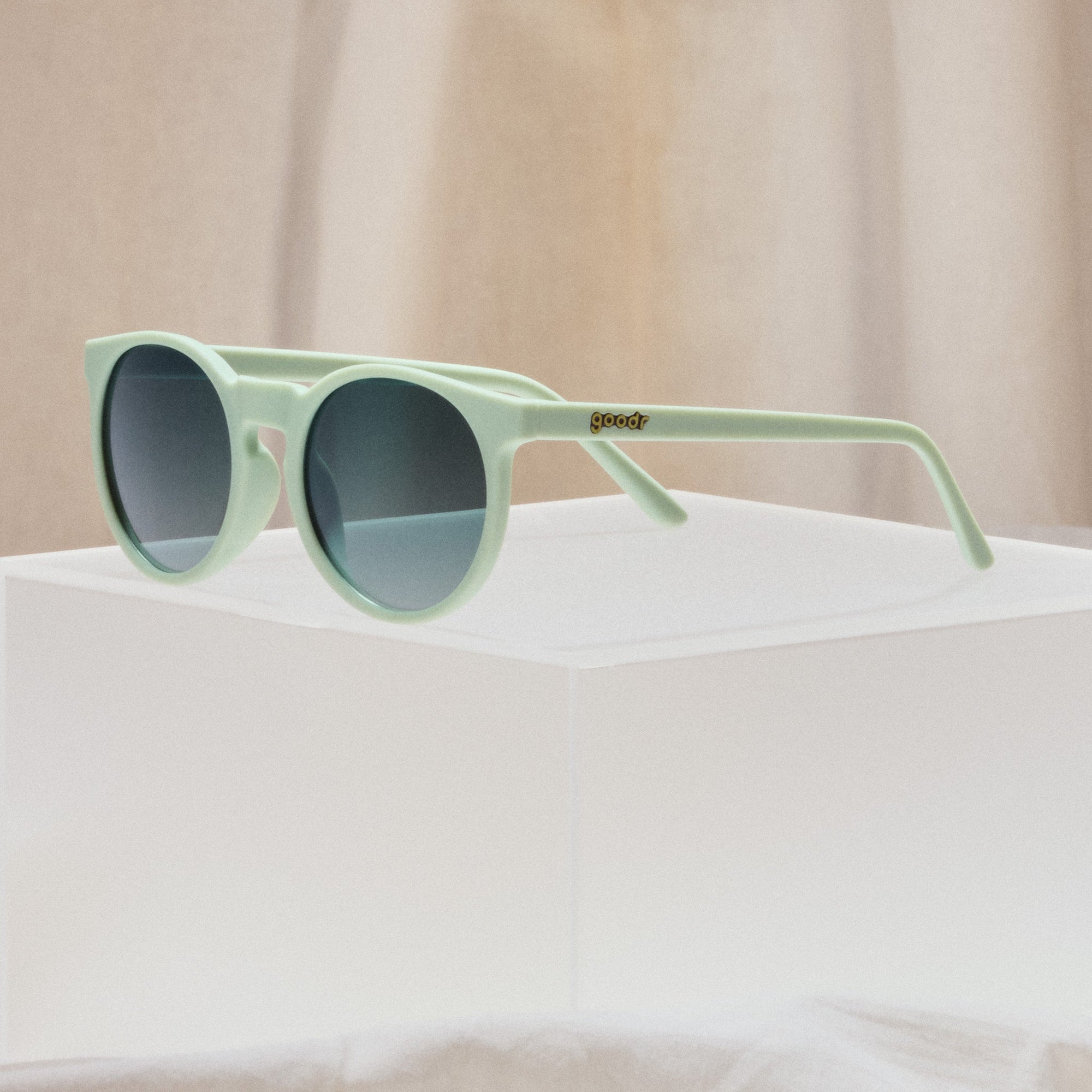 Round sunglasses with sage green frames and dark gradient lenses on white surface