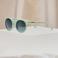 Round sunglasses with sage green frames and dark gradient lenses on white surface