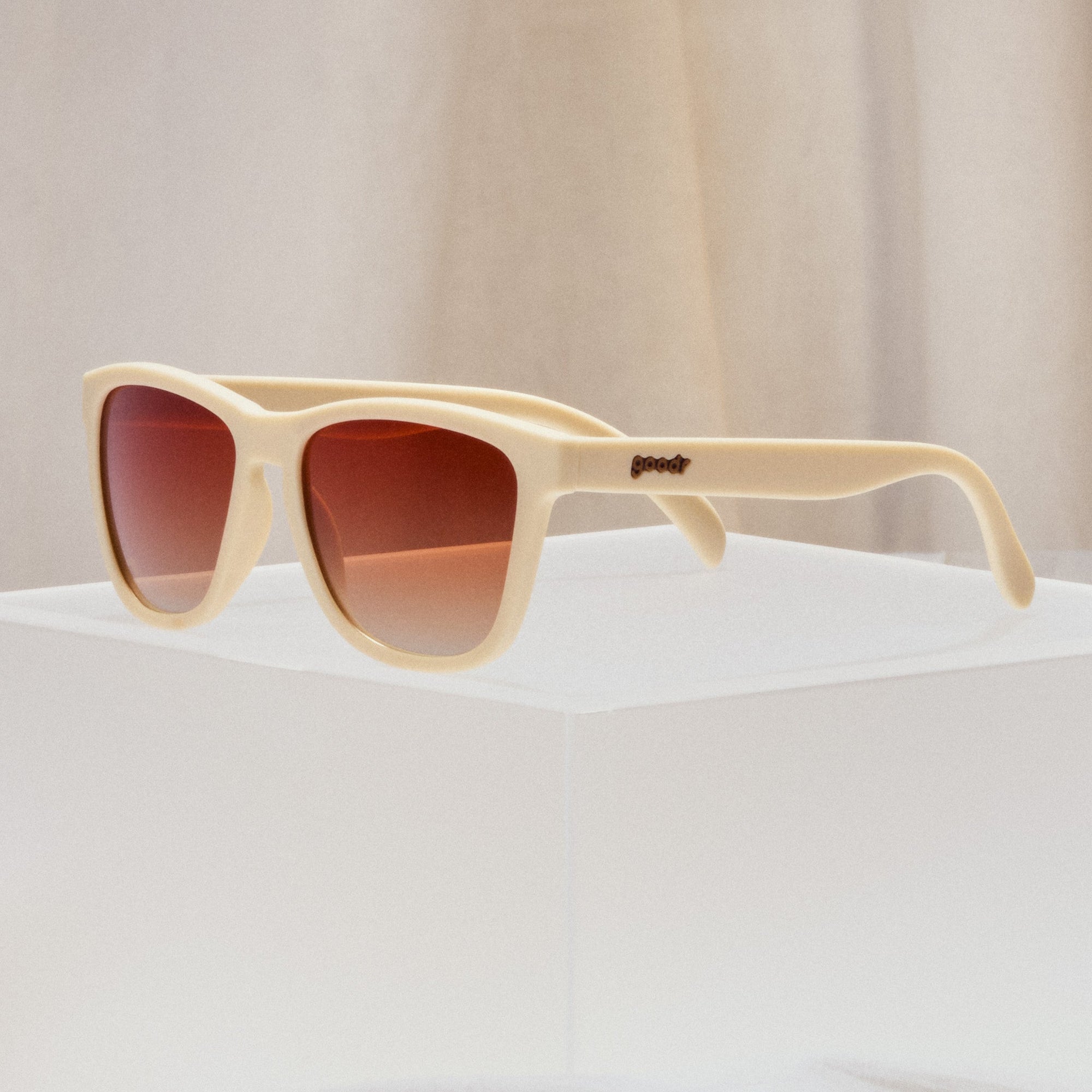 Cream colored sunglasses with gradient orange-brown lenses on white surface
